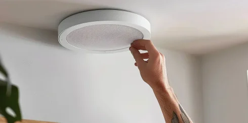 a person fitting a sleek, white ceiling speaker seamlessly into a wallboard, showcasing a modern and elegant home audio setup.